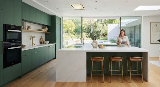 Modern modular kitchen with emerald green cabinetry and a white quartz waterfall island