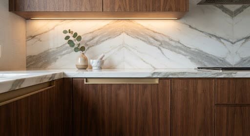 Bespoke walnut joinery with champagne brass hardware, a bookmatched marble countertop and warm cove lighting